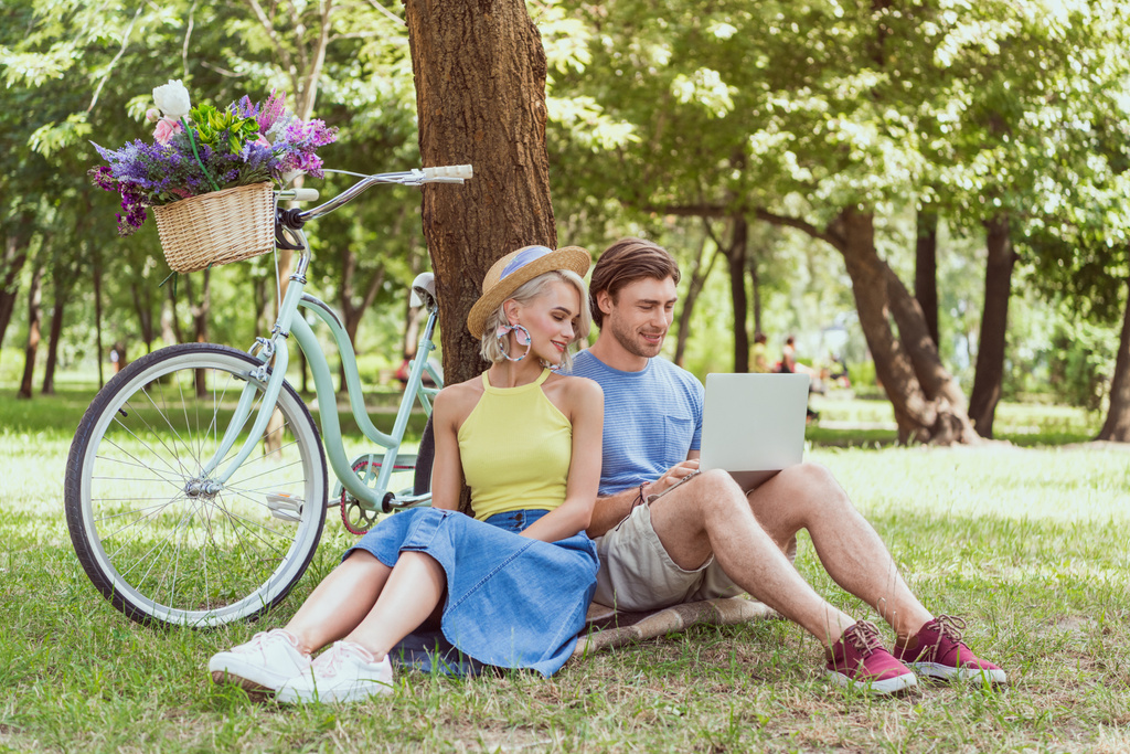 casal sentado perto da árvore no parque e usando laptop
 - Foto, Imagem