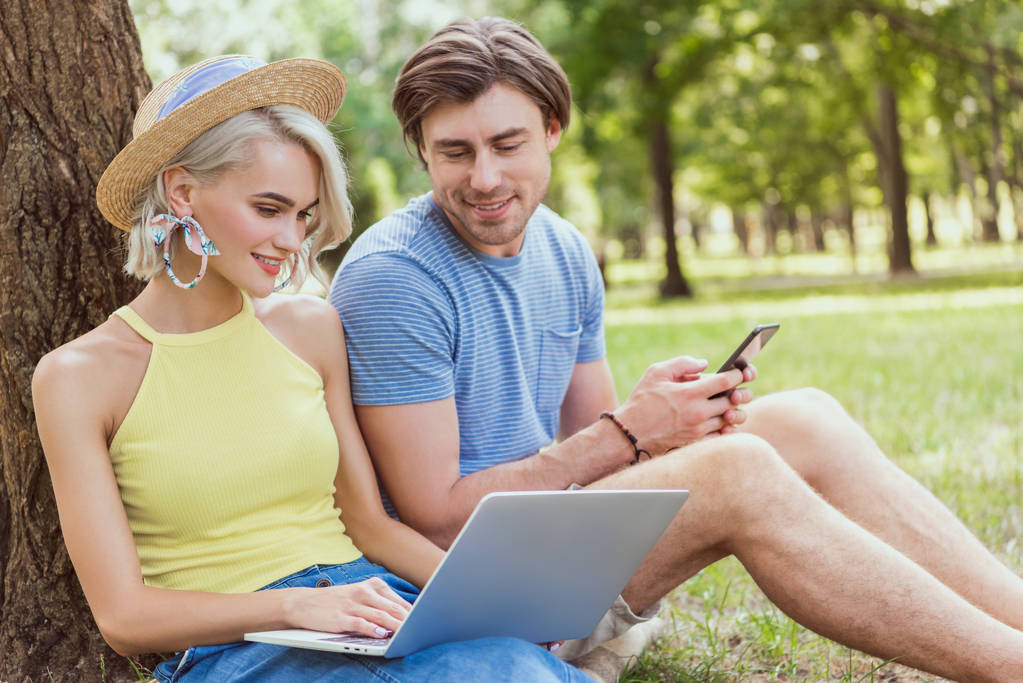 Paar schaut auf Laptop und sitzt im Park auf Gras - Foto, Bild
