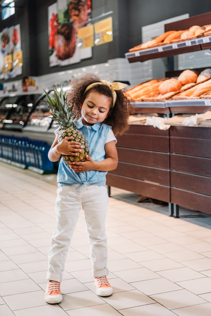 pequeno garoto afro-americano de pé com abacaxi no supermercado
  - Foto, Imagem