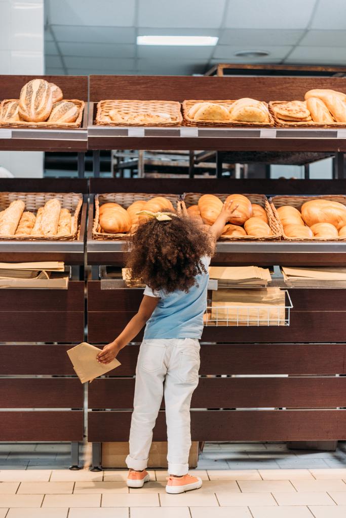 vista trasera del niño pequeño que elige el pan en la tienda de comestibles
  - Foto, Imagen