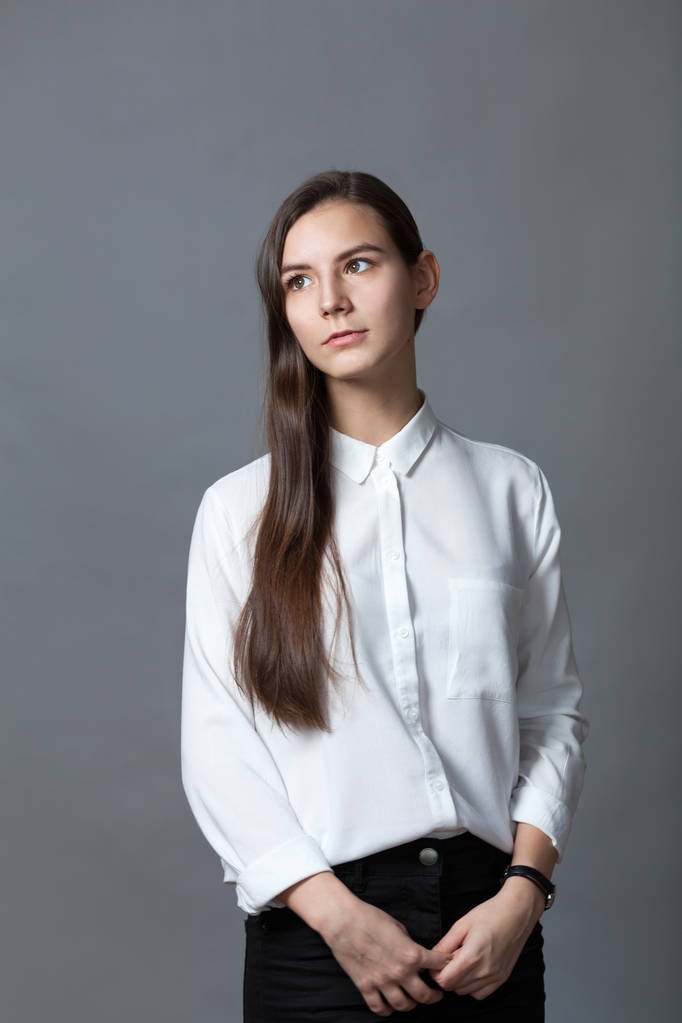 Retrato de adolescente colegiala feliz agradable en camisa blanca sobre fondo gris, estudio
 - Foto, Imagen