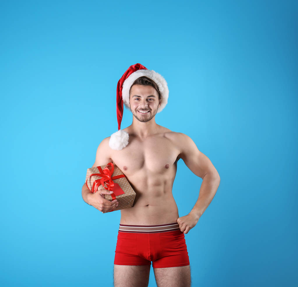 hemdlos sexy junge Weihnachtsmann mit Geschenk auf farbigem Hintergrund - Foto, Bild