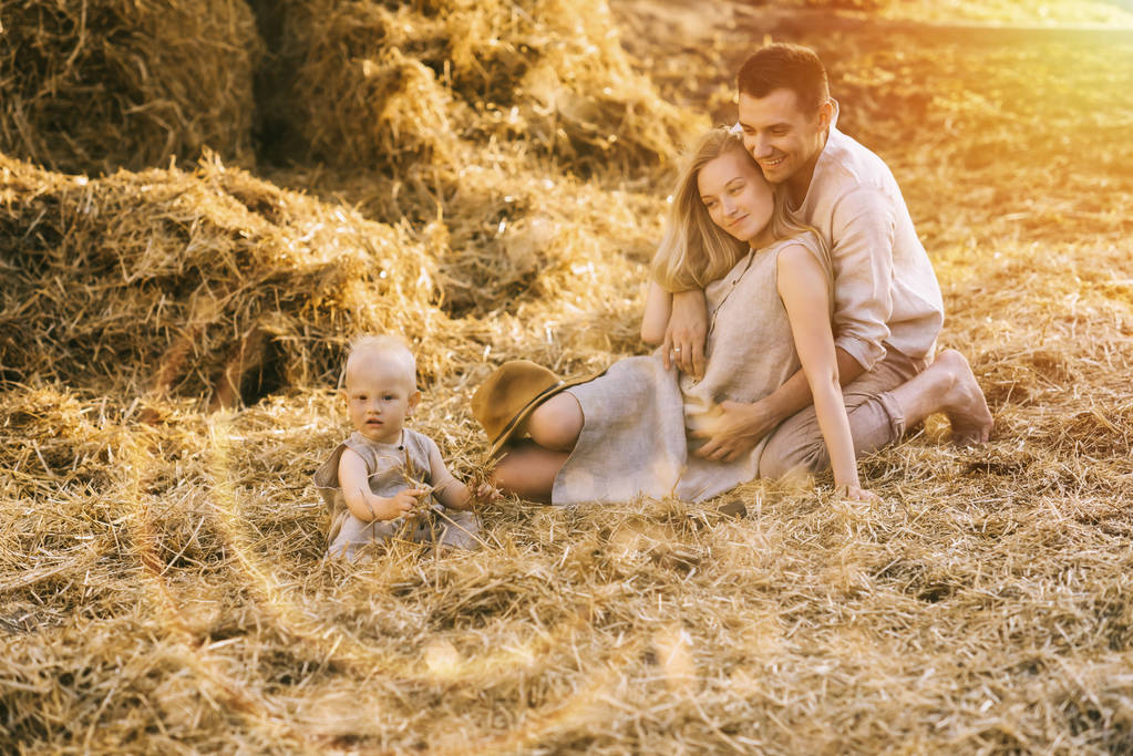 parents and little son in linen clothing resting on hay at countryside - Photo, Image