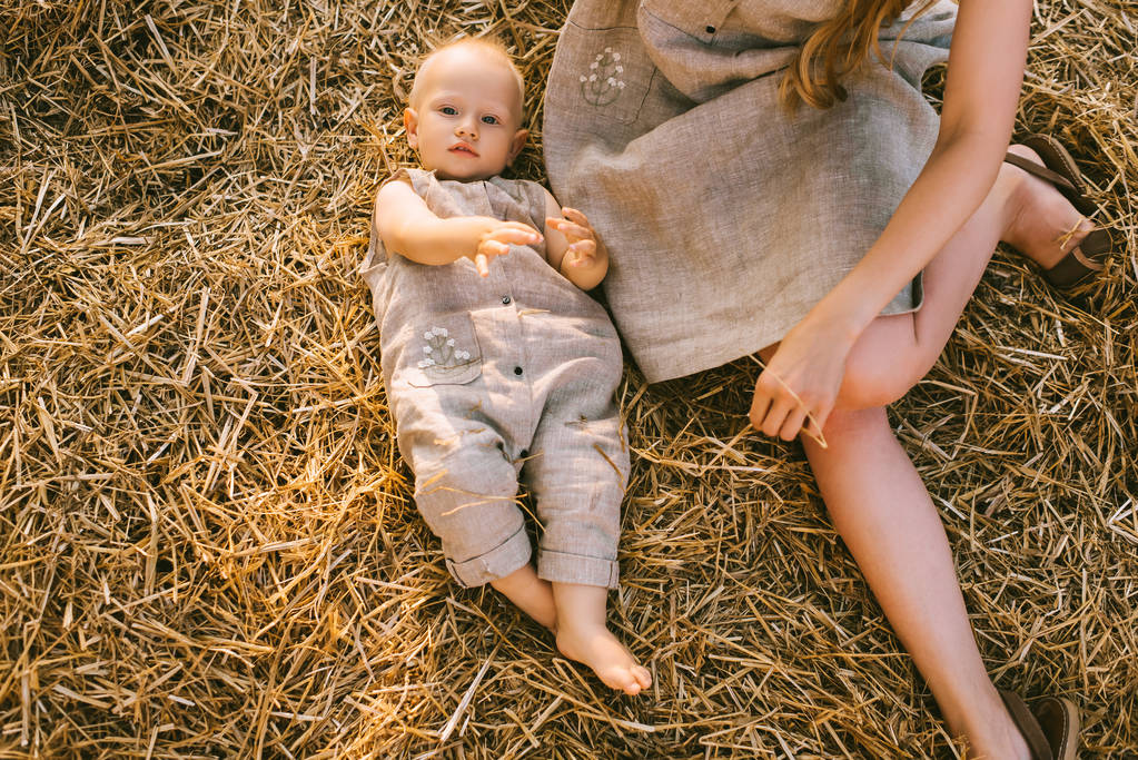 overhead view of mother and son in linen clothing resting on hay together - Photo, Image