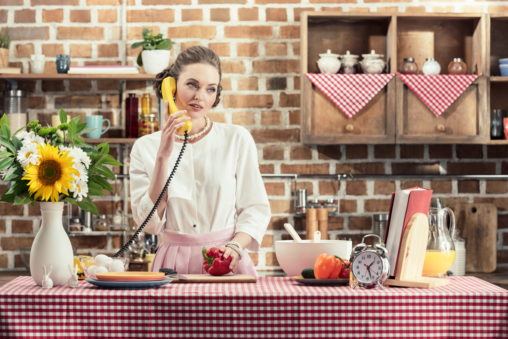 красива доросла домогосподарка розмовляє по телефону під час приготування їжі на кухні
 - Фото, зображення