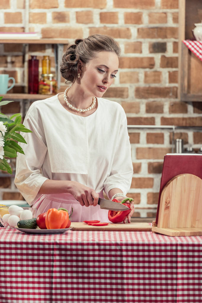 stylish adult housewife in vintage clothes cutting tomato at kitchen - Photo, Image