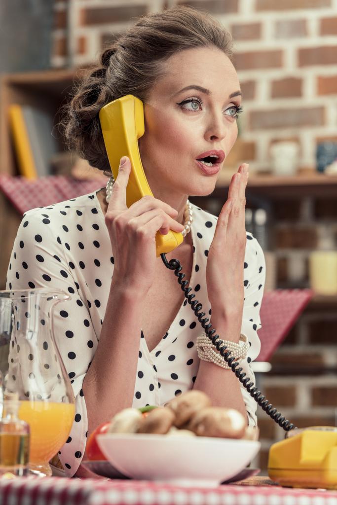 σοκαρισμένος ενηλίκων νοικοκυρά μιλάμε από vintage ενσύρματο τηλέφωνο στην κουζίνα - Φωτογραφία, εικόνα