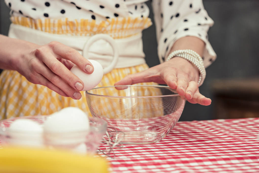 обрезанный снимок домохозяйки, разбивающей яйцо в миску для омлета
 - Фото, изображение