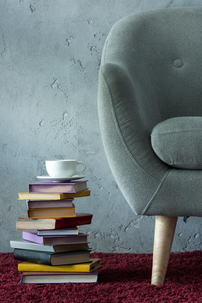 stack of books and cup of coffee on burgundy carpet near grey armchair in office - Photo, Image