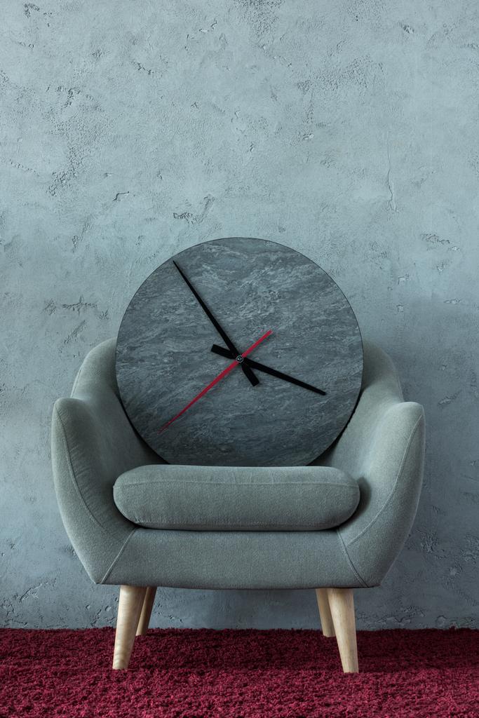 сіре крісло з годинником на бордовому килимі біля сірої стіни в офісі
 - Фото, зображення