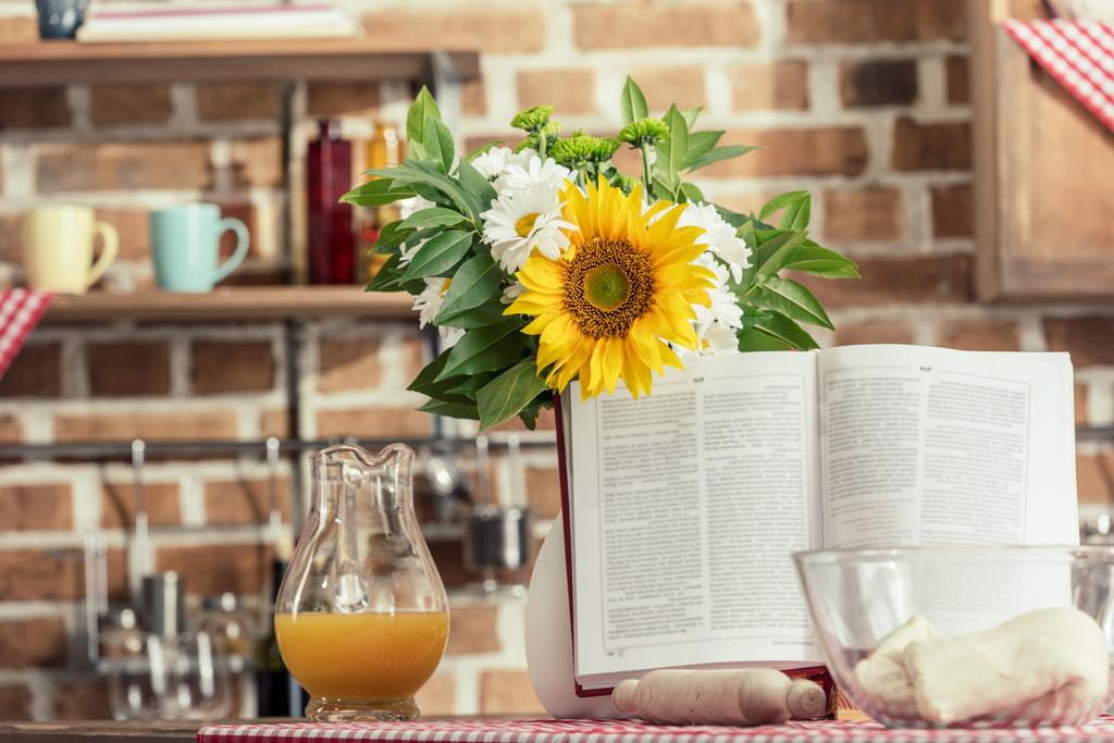 recipe book and bouquet of flowers on cooking table at kitchen - Photo, Image