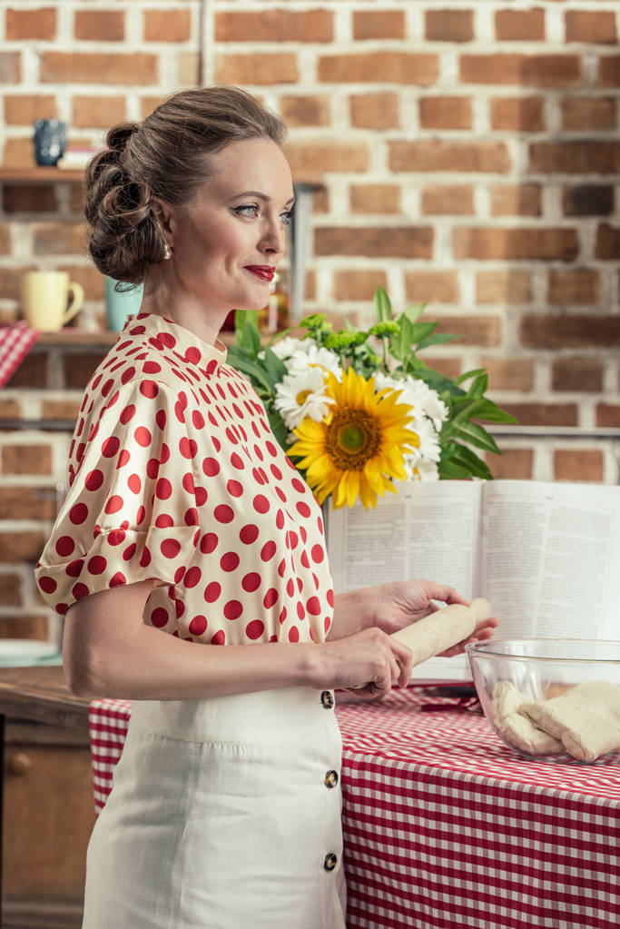 oklava uzak mutfak at hamur hazırlık sırasında seyir ile güzel yetişkin ev kadını yan görünüm - Fotoğraf, Görsel