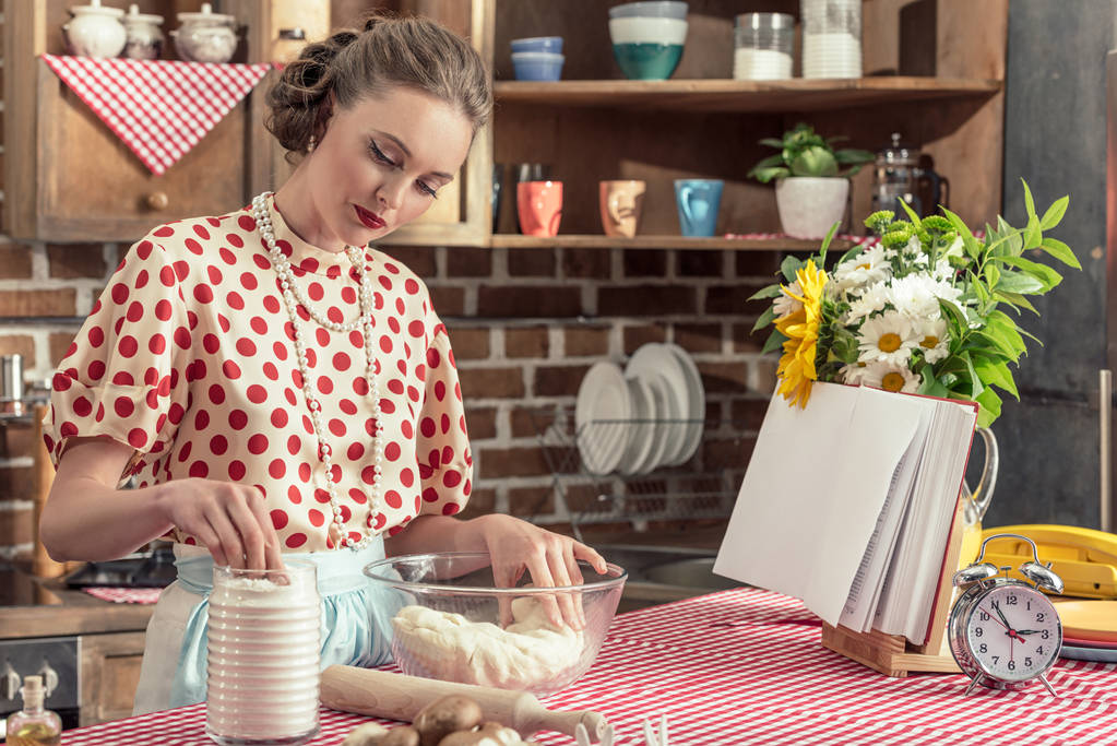 aantrekkelijke volwassen huisvrouw, kneden van deeg in de kom op keuken - Foto, afbeelding