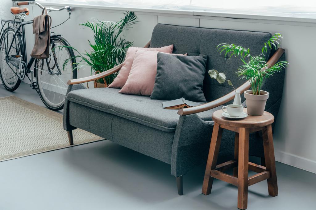 szürke kanapé párnák, kerékpár, a nappali fala közelében - Fotó, kép