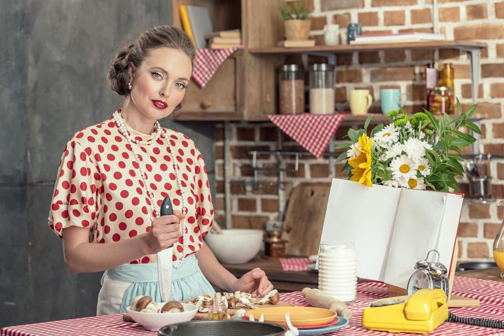 bela dona de casa adulta com faca cozinhar e olhando para a câmera na cozinha
 - Foto, Imagem