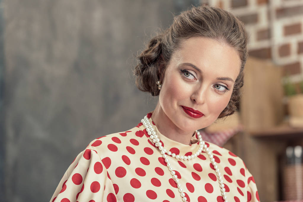 Close-up portret van prachtige volwassen vrouw in vintage polka dot shirt en parel ketting op zoek weg - Foto, afbeelding