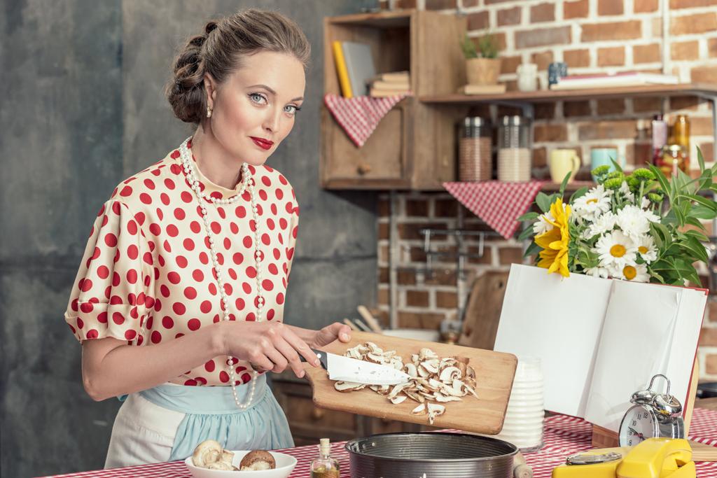 piękna gospodyni dorosłych wylewanie pokrojonych w plasterki pieczarek do pieczenia trey na ciasto i patrząc na kamery w kuchni - Zdjęcie, obraz