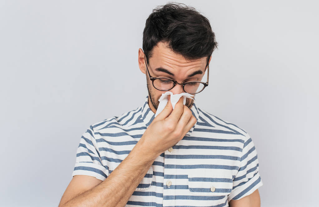 Closeup portrait of Caucasian sick male wearing striped shirt and glasses, caught cold and sneezing into tissue. Man have headache, virus against white background. Healthy, medicine concept. - Photo, Image