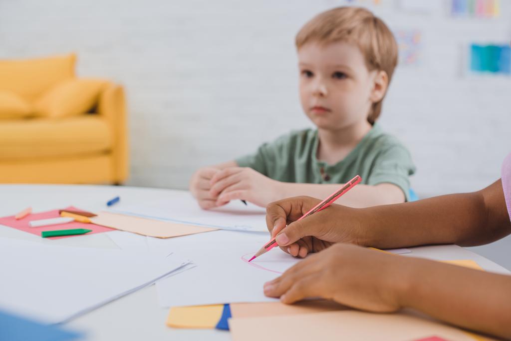 vista parziale di bambini in età prescolare multiculturale a tavola con carte e matite in classe
 - Foto, immagini