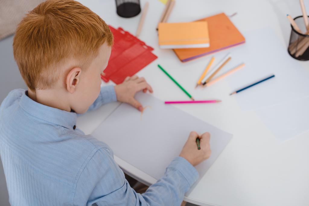 high angle view of red hair boy drawing picture with pencils at table  - Photo, Image