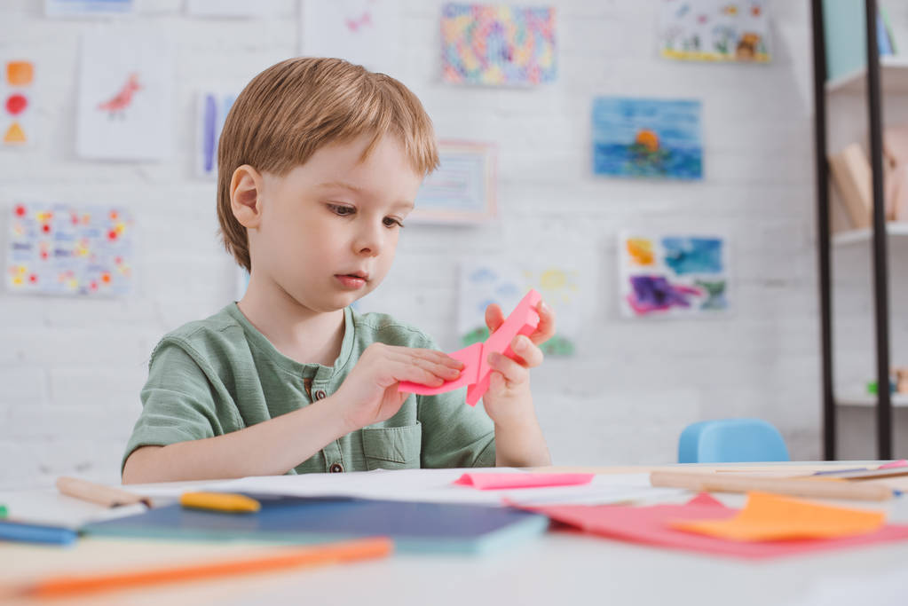roztomilý preschooler s na jasně růžovém papíru u stolu v učebně - Fotografie, Obrázek