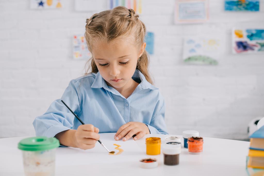 portrait of adorable focused child drawing picture with paints and brush at table - Photo, Image