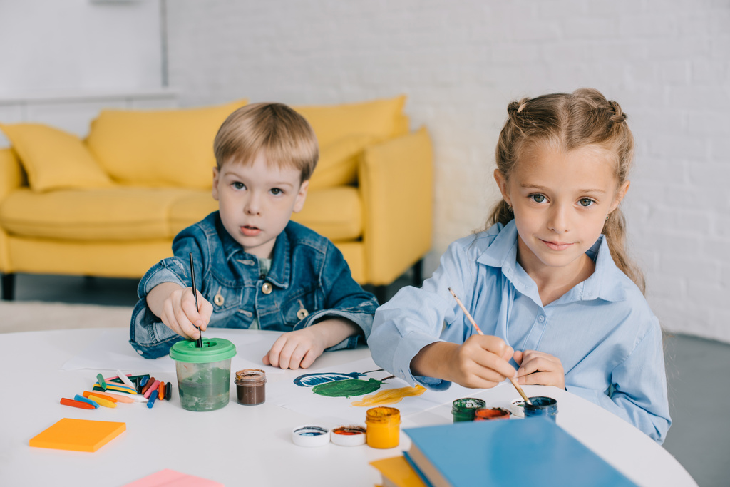 портрет дошкольников, рисующих картины красками и кисточками за столом в классе
 - Фото, изображение