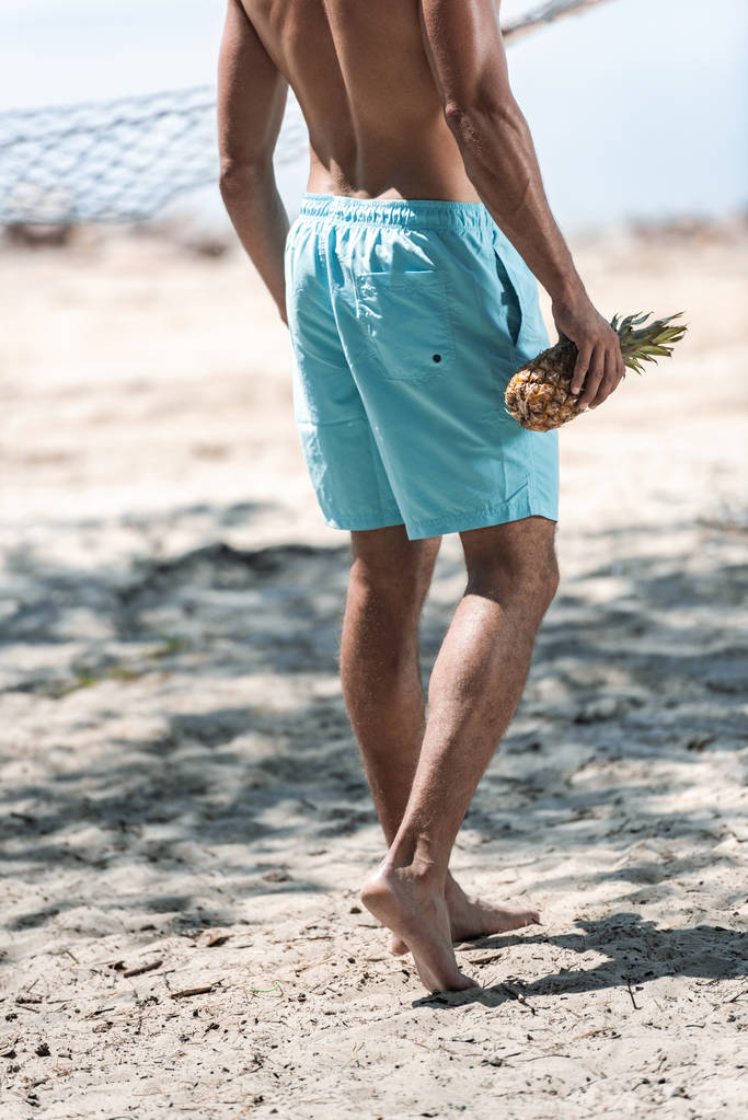 cropped view of man holding fresh pineapple on beach - Photo, Image