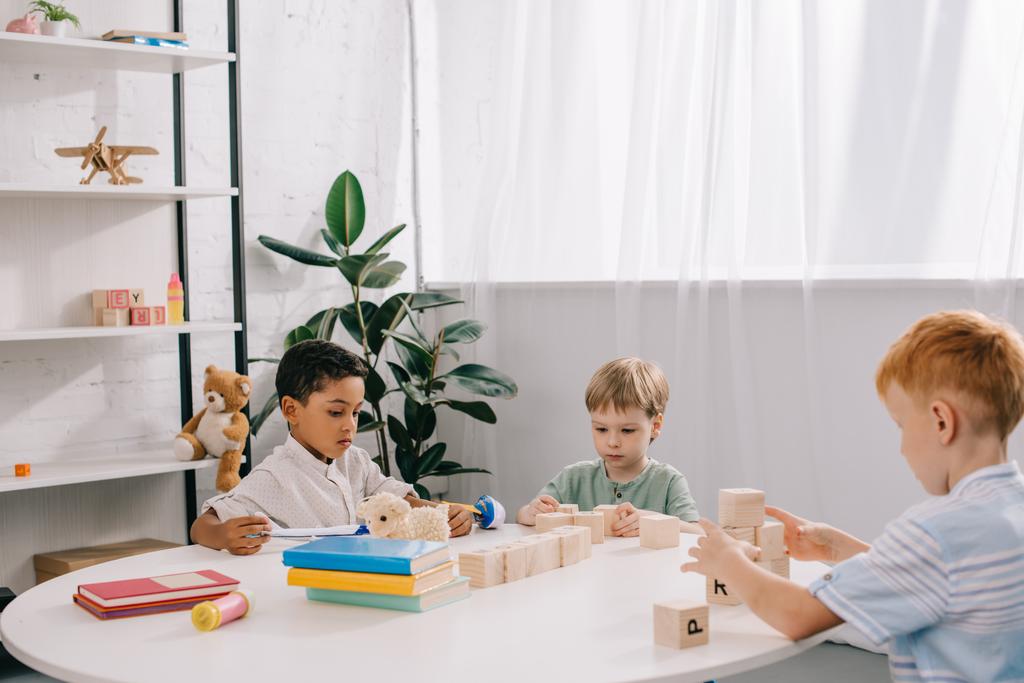 niños pequeños multiculturales jugando con bloques de madera en la mesa en el aula
 - Foto, imagen