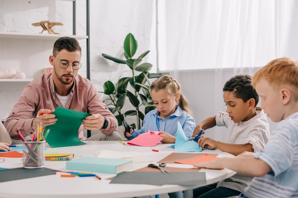 enseignant et enfants d'âge préscolaire multiracial coupant des papiers colorés avec des ciseaux en classe
  - Photo, image