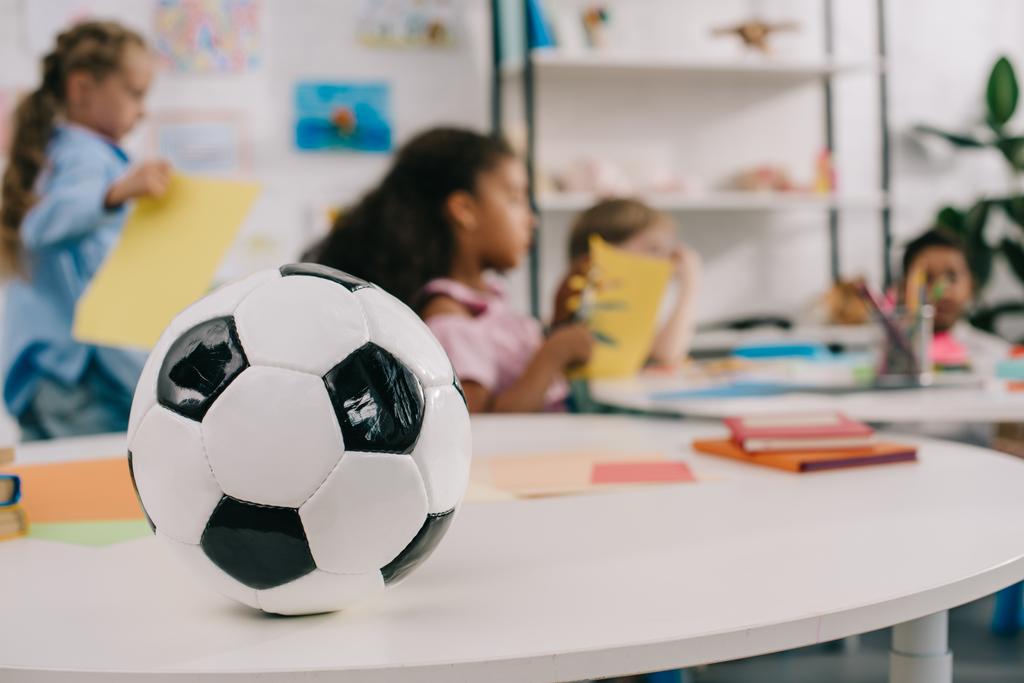 Selektiver Fokus des Fußballs auf Tisch und multirassische Vorschulkinder im Klassenzimmer - Foto, Bild