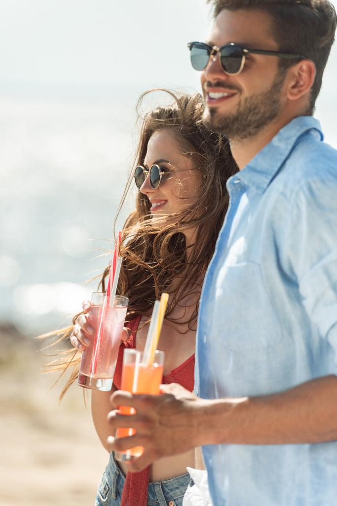 schönes Paar mit Sonnenbrille, Cocktails in der Hand und Blick aufs Meer - Foto, Bild