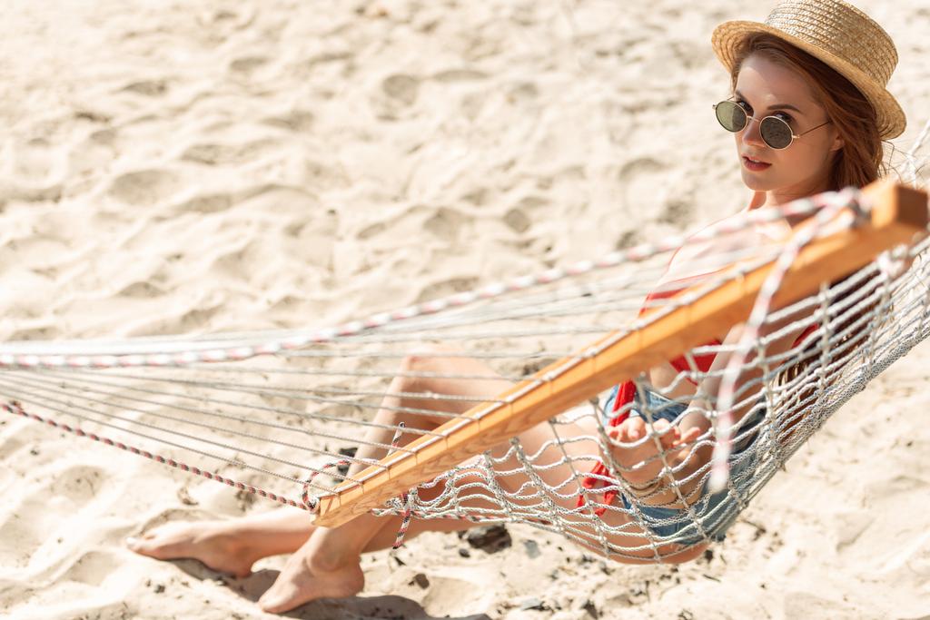 Atrakcyjna dziewczyna w słomkowym kapeluszu, odpoczynek w hamaku na piaszczystej plaży - Zdjęcie, obraz