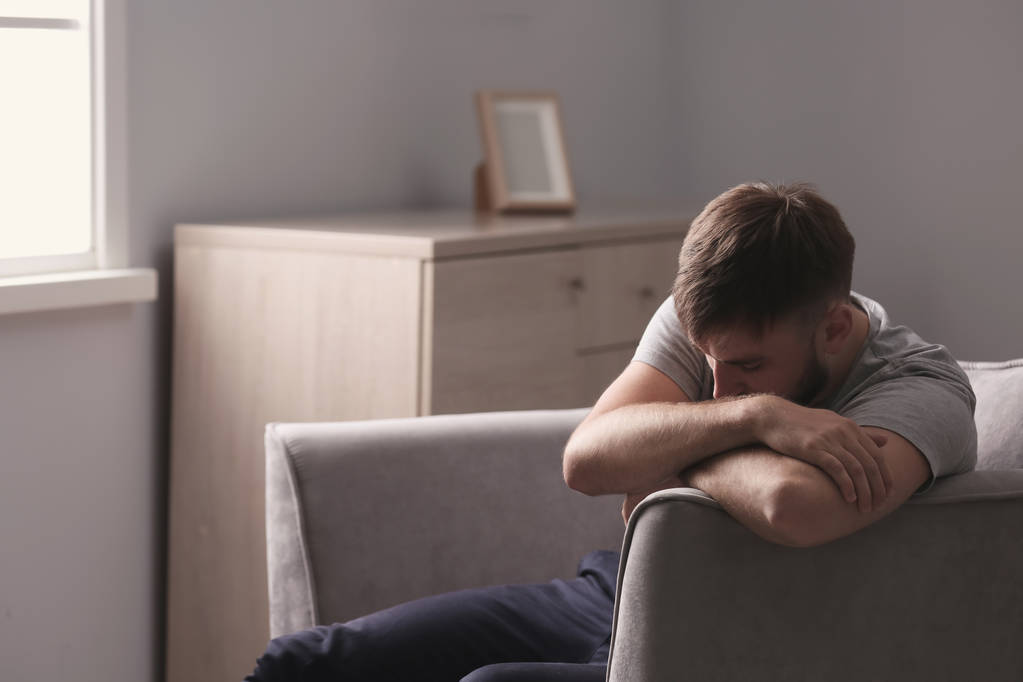 Deprimido jovem sentado em poltrona em casa
 - Foto, Imagem