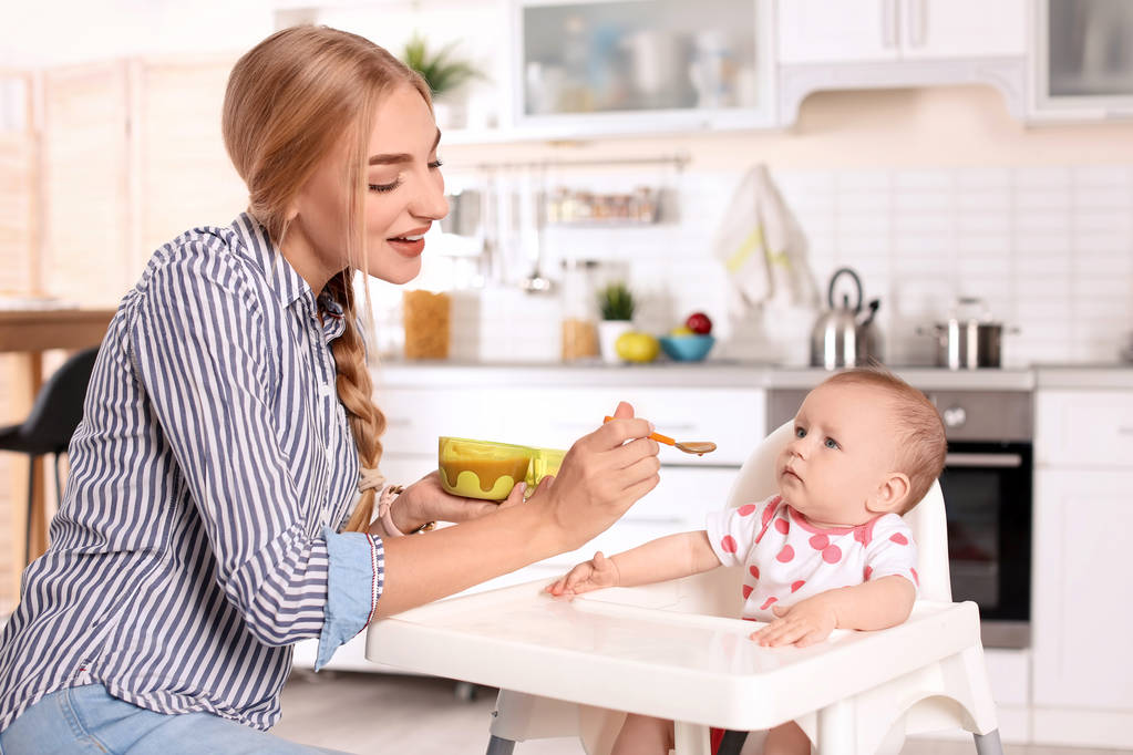 Mulher alimentando seu filho em cadeira alta dentro de casa. Alimentos saudáveis para bebés
 - Foto, Imagem