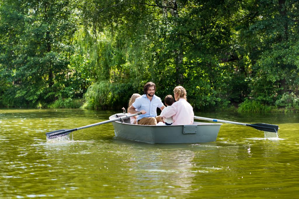 gelukkige jonge familie samen tijd doorbrengen in de boot op de rivier in het park - Foto, afbeelding