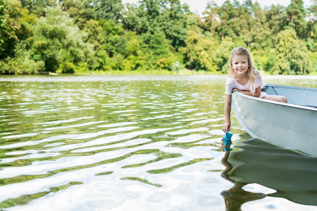 Прекрасный маленький ребенок запускает бумагу оригами лодка во время плавания в лодке на озере
 - Фото, изображение