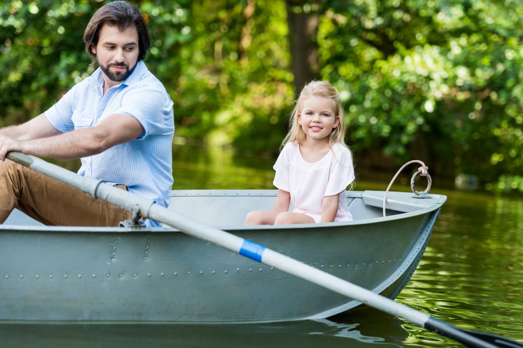 vista lateral del padre y la hija a caballo barco en el lago en el parque
 - Foto, Imagen