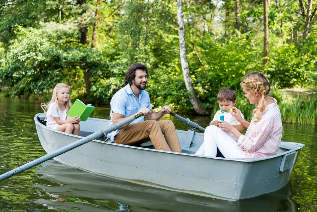 glimlachend jonge familie riding boot op de rivier in het park - Foto, afbeelding