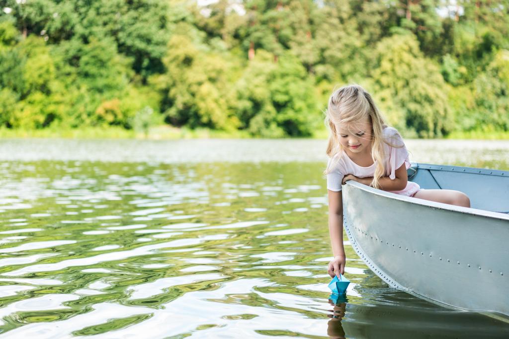happy little child launching paper origami boat while floating in boat on lake - Photo, Image
