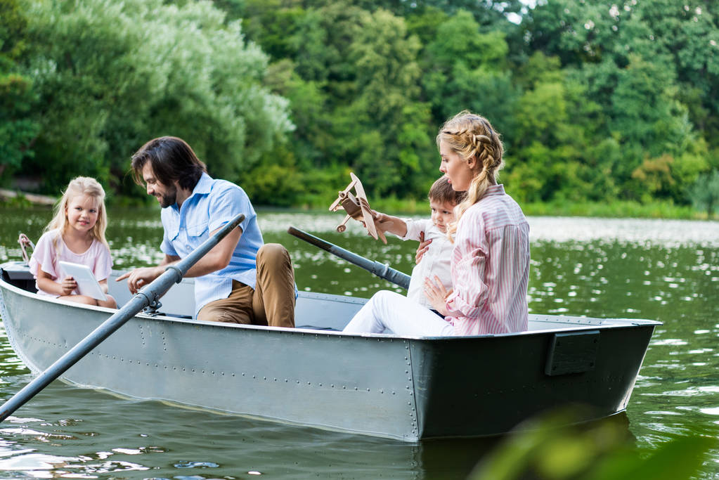 belle jeune famille équitation bateau sur le lac, en utilisant la tablette et jouer avec l'avion jouet
 - Photo, image