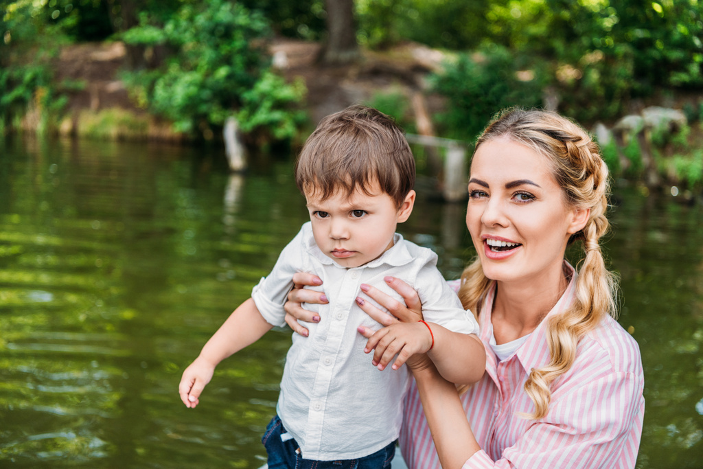 happy mother with sad little son in front of water surface - Photo, Image