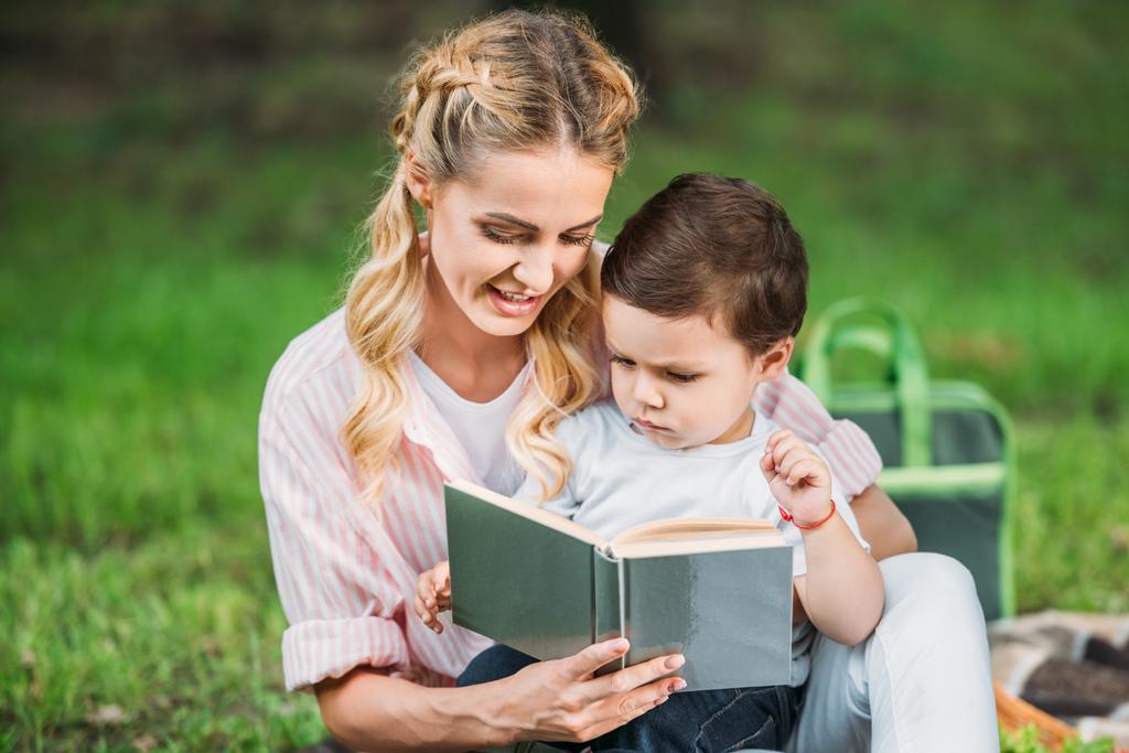 Gelukkig moeder met zoon leesboek op park - Foto, afbeelding
