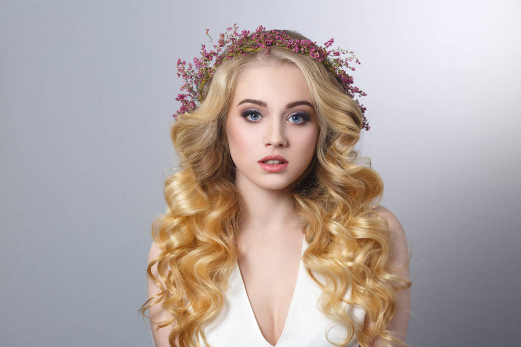 Portret van de schoonheid van een mooi blond meisje met chique krullen en een krans van heather geïsoleerd op een grijze achtergrond. - Foto, afbeelding