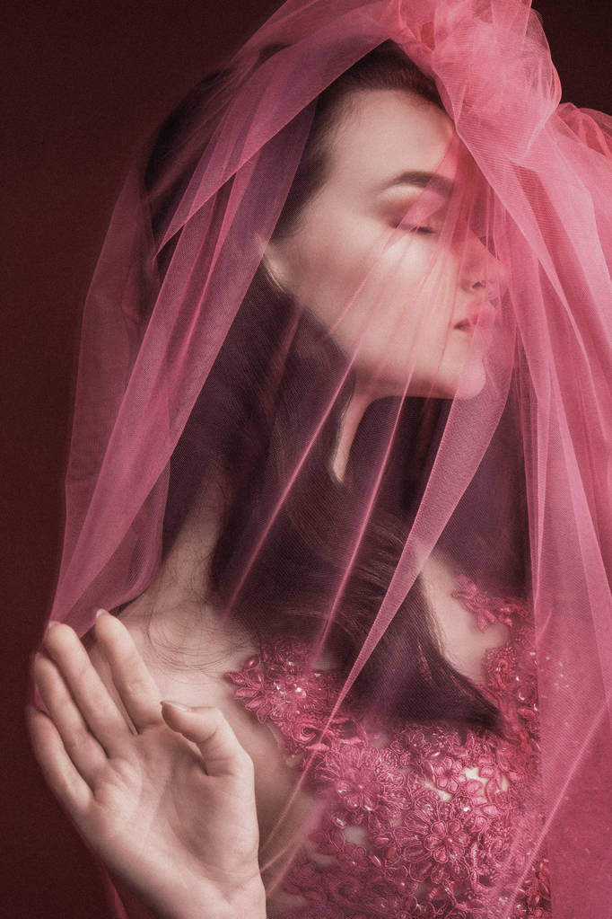 Hermosa modelo de niña en un vestido rojo largo sobre un fondo de vino de color. Disparo a través de un paño rosa transparente
. - Foto, imagen