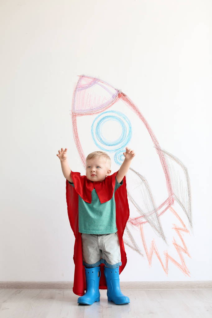 entzückendes kleines Kind spielt Astronautin nahe Wand mit Zeichnung von Raumschiff drinnen - Foto, Bild