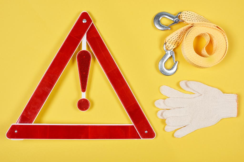 bovenaanzicht van waarschuwing driehoek verkeersbord, handschoenen en auto tow rope geïsoleerd op geel - Foto, afbeelding