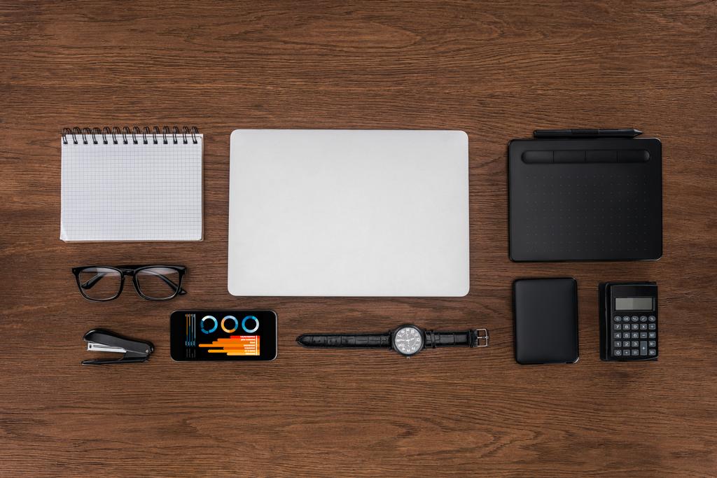 Ansicht des Arbeitsplatzes mit geordnetem leeren Lehrbuch, Laptop, Armbanduhr und Smartphone mit Grafik auf dem Bildschirm - Foto, Bild