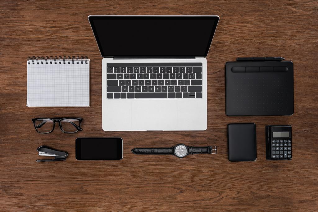bovenaanzicht van werkplek met gearrangeerde lege leerboek, smartphone, horloge en laptop met leeg scherm - Foto, afbeelding