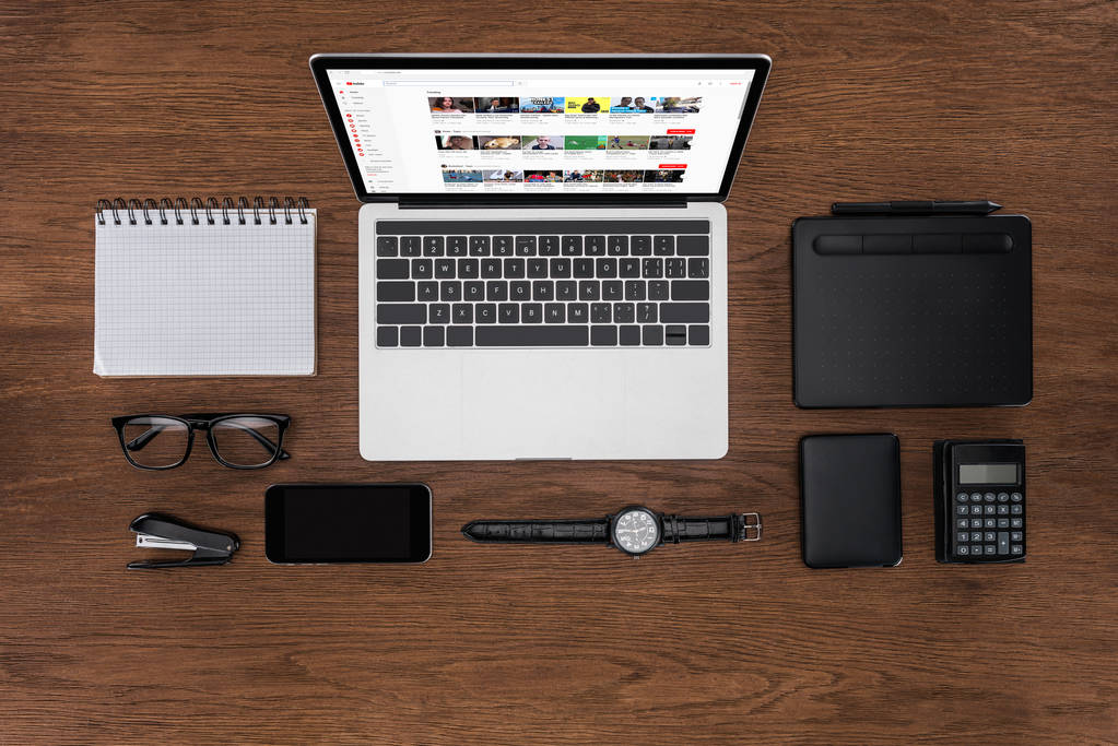 bovenaanzicht van werkplek met gearrangeerde lege leerboek, smartphone, horloge en laptop met youtube op scherm - Foto, afbeelding
